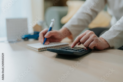Close up of hands using calculator and writing on notebook with miniature car and house. Financial planning, calculating property mortgage, auto loan, and monthly expenses management.