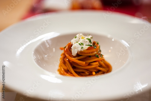 Spaghetti in tomato sauce with burrata on white plate in intimate romantic restaurant