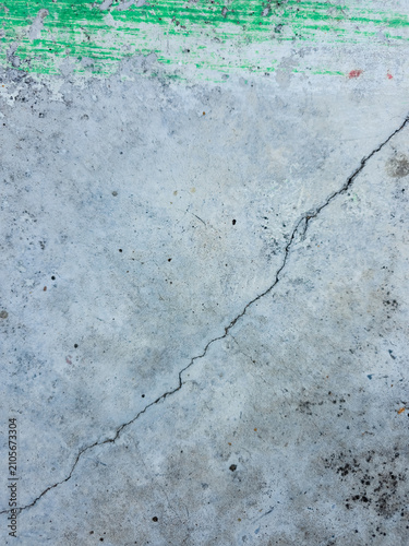 Diagonal crack across a gray concrete floor surface with green paint mark at the top