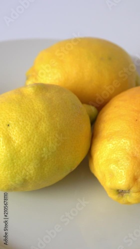 Three lemons sit on a plate in good light. vertical video