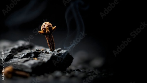 Incense stick burning with smoke rising from charcoal in dark setting
