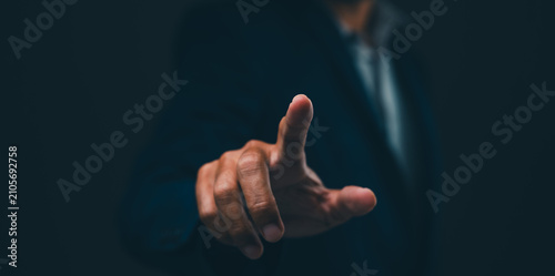 Принти на полотні A person in a dark suit points forward with their index finger against a dark background, emphasizing focus and interaction