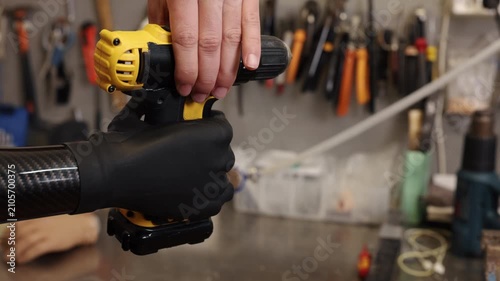 yellow drill, hand prosthesis, adaptive technology. Prosthetic hand securely grips drill, highlighting precision and effectiveness in workshop setting.