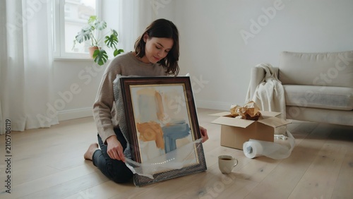 Woman Sitting on Floor Unpacking Framed Artwork in Bright Living Room