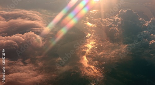 Sunlight streams through clouds, casting rainbow prisms over a distant, hazy landscape
