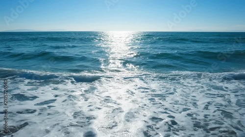 Tranquil ocean waves crash onto the sandy beach with bright sunlight reflection a peaceful summer coastal scene
