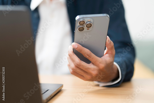 Hands of business man holding mobile phone during using laptop computer on table