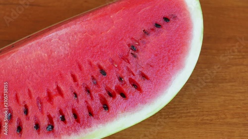 A slice of ripe red watermelon rotating on a textured wooden table surface with a static camera view. High speed fps footage for summer food commercial, organic fruit and refreshing dessert video. 