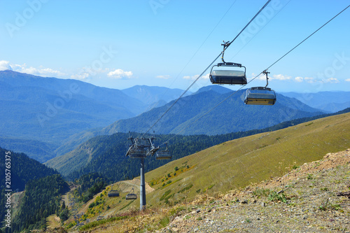 A modern, empty chairlift suspended by cables and moving high above the mountain landscape.