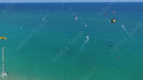 Aerial view of many people riding the waves on the weekend. Colorful parachutes of surfers against the blue sea and sky. Dynamic kitesurfing action in the ocean. Kiteboarding.