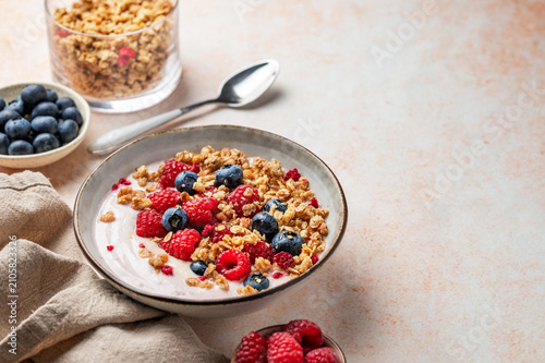 Natural greek yogurt with granola, blueberry and raspberry in a bowl on a light textured background