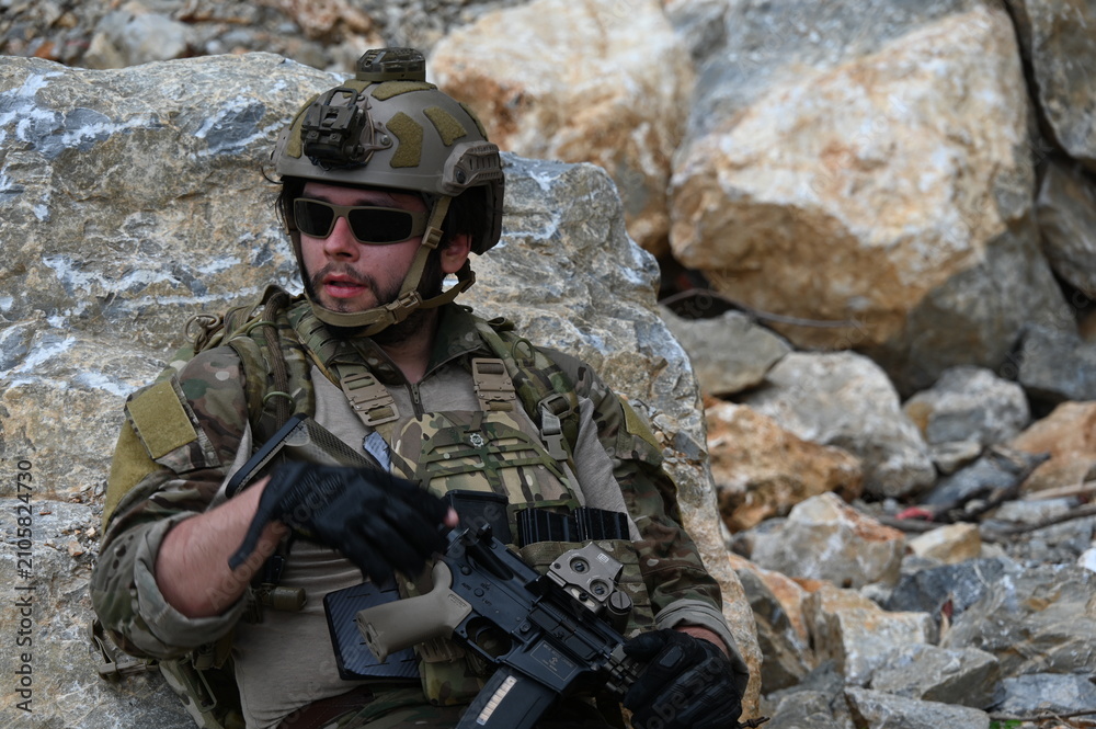 Obraz premium Focused military infantry soldier lying prone on rugged rocky terrain aiming a tactical assault rifle during a dangerous combat training mission for national defense and special security.