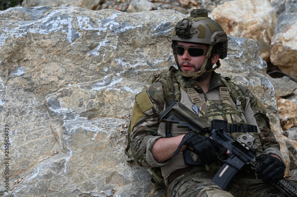 Obraz premium Focused military infantry soldier lying prone on rugged rocky terrain aiming a tactical assault rifle during a dangerous combat training mission for national defense and special security.