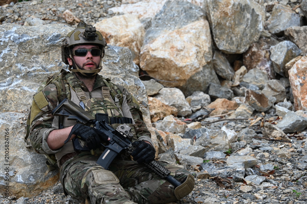 Obraz premium Focused military infantry soldier lying prone on rugged rocky terrain aiming a tactical assault rifle during a dangerous combat training mission for national defense and special security.