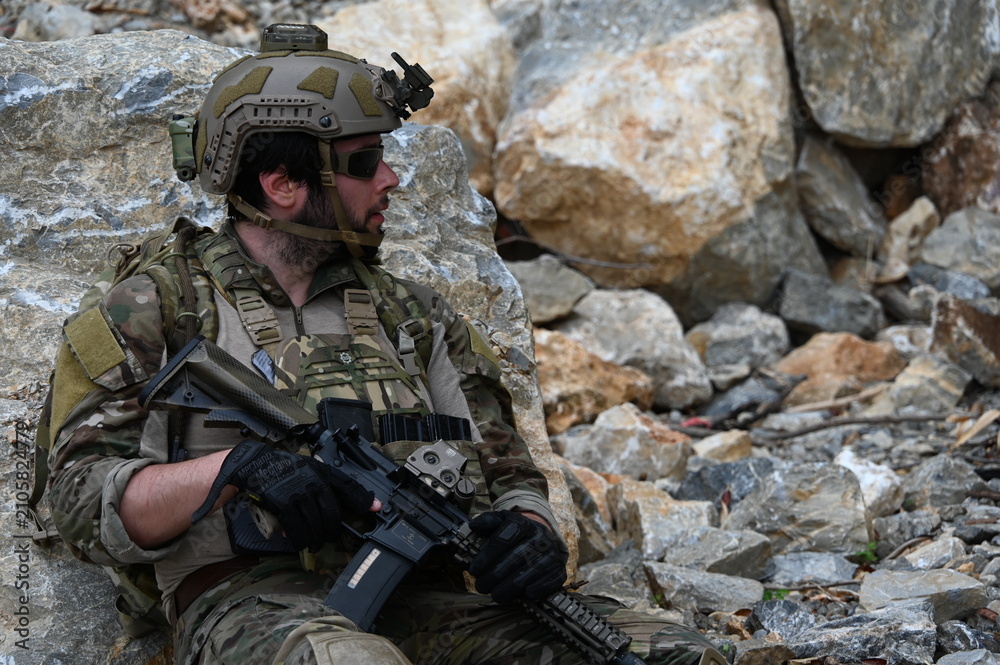 Obraz premium Focused military infantry soldier lying prone on rugged rocky terrain aiming a tactical assault rifle during a dangerous combat training mission for national defense and special security.
