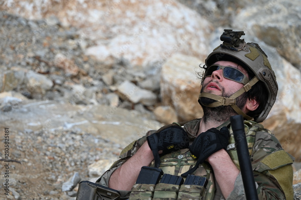 Obraz premium Focused military infantry soldier lying prone on rugged rocky terrain aiming a tactical assault rifle during a dangerous combat training mission for national defense and special security.