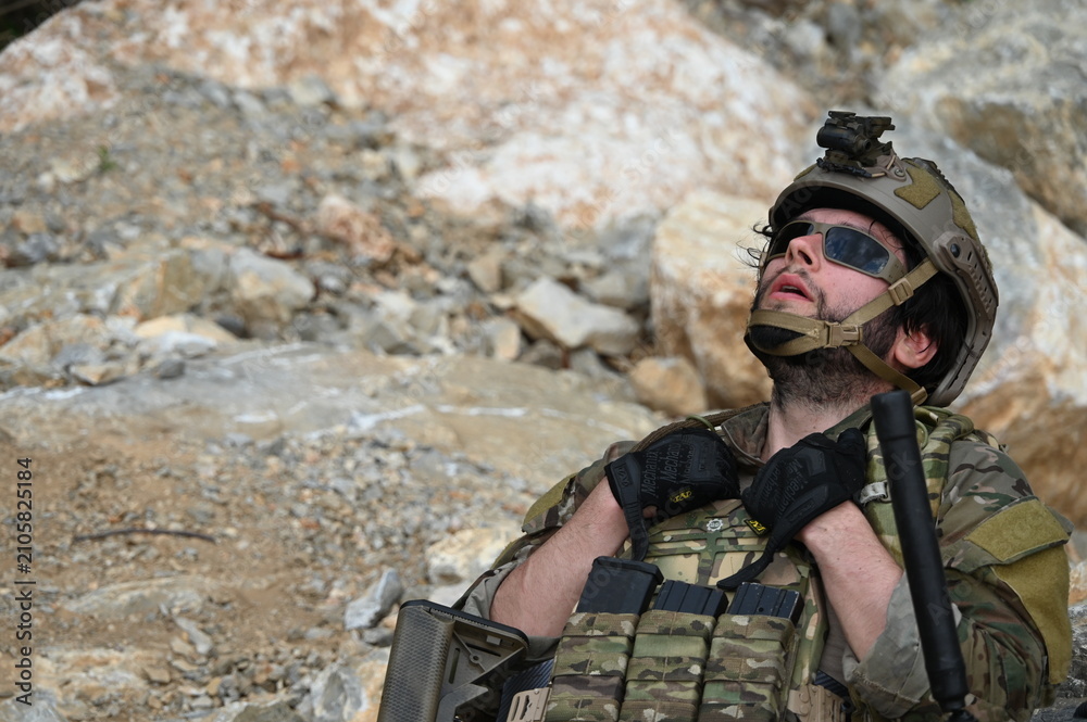 Obraz premium Focused military infantry soldier lying prone on rugged rocky terrain aiming a tactical assault rifle during a dangerous combat training mission for national defense and special security.