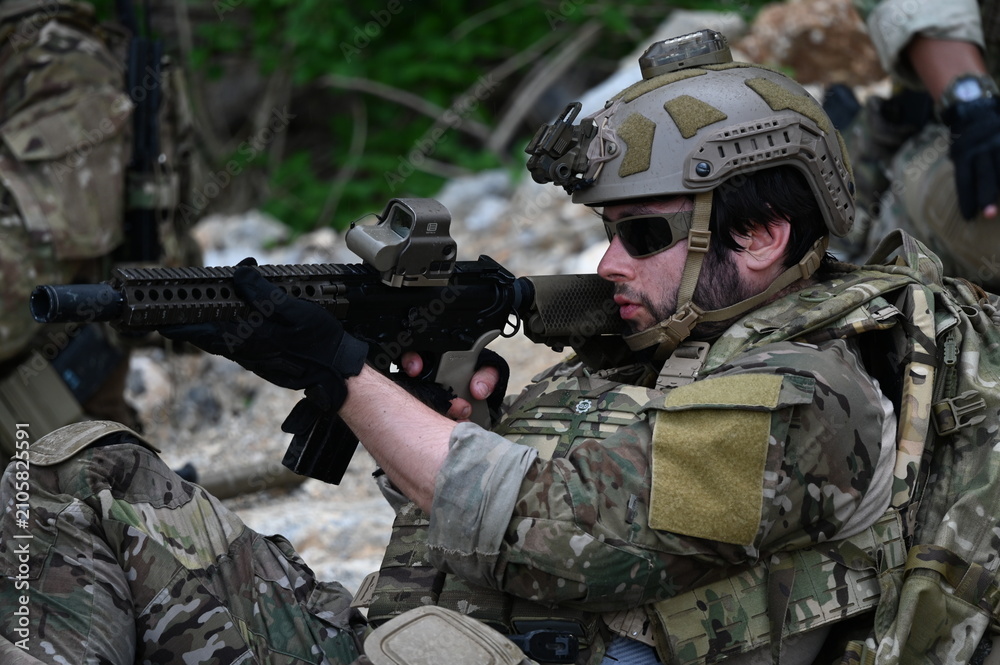 Obraz premium Focused military infantry soldier lying prone on rugged rocky terrain aiming a tactical assault rifle during a dangerous combat training mission for national defense and special security.