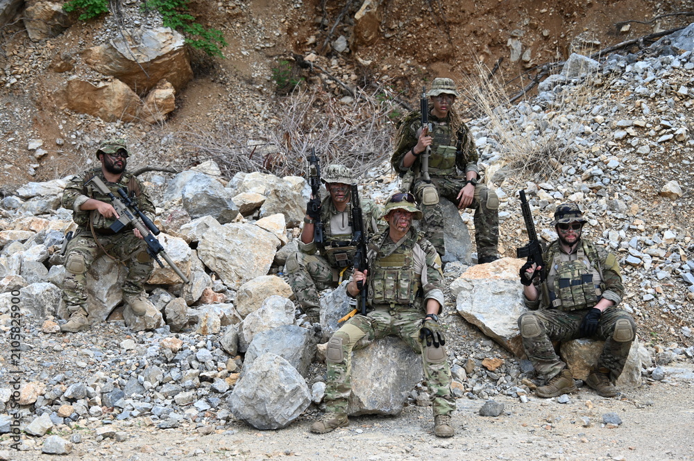 Obraz premium Dedicated squad of professional armed military soldiers walking in patrol formation along a rugged rocky mountain cliff during a dangerous tactical combat mission or outdoor training exercise.