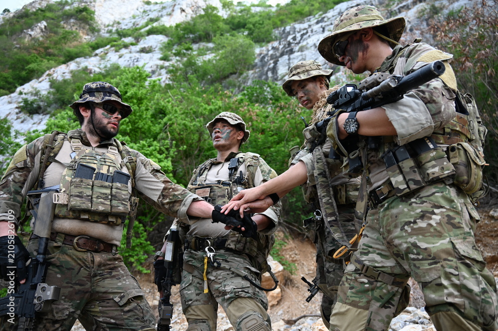 Fototapeta premium Tactical team in camouflage gear checks a navigation device during outdoor training in rocky terrain. Concept of teamwork, communication, security, and field operations.