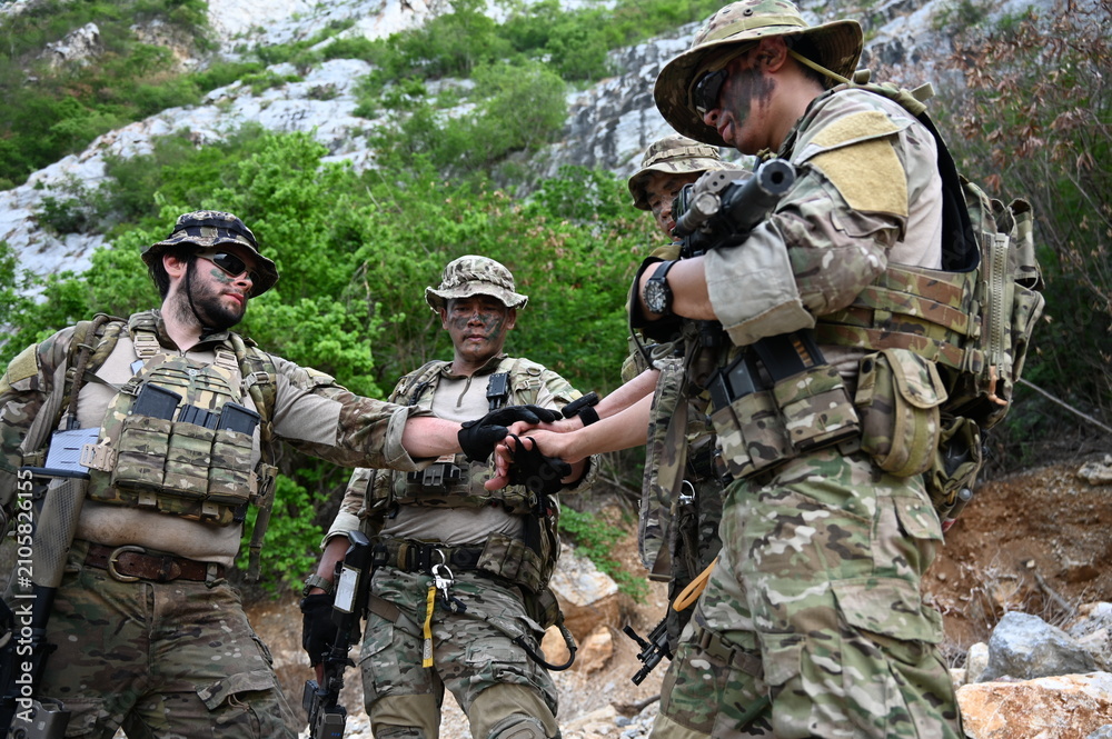 Fototapeta premium Tactical team in camouflage gear checks a navigation device during outdoor training in rocky terrain. Concept of teamwork, communication, security, and field operations.