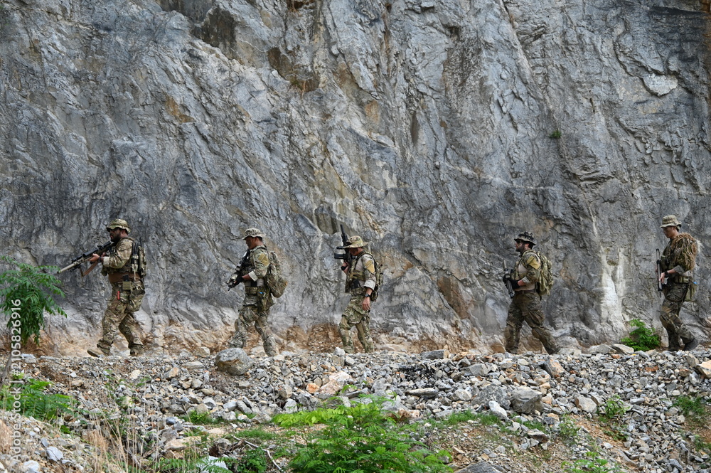 Obraz premium Dedicated squad of professional armed military soldiers walking in patrol formation along a rugged rocky mountain cliff during a dangerous tactical combat mission or outdoor training exercise.