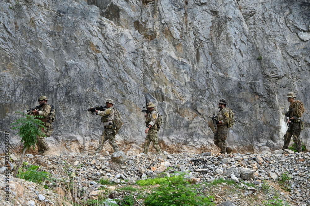 Obraz premium Dedicated squad of professional armed military soldiers walking in patrol formation along a rugged rocky mountain cliff during a dangerous tactical combat mission or outdoor training exercise.