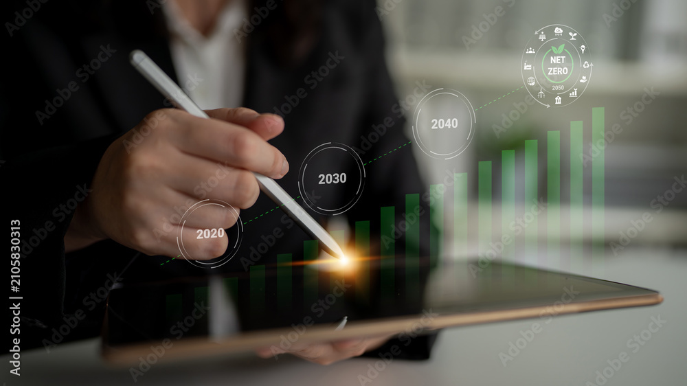 Obraz premium A business professional uses a stylus on a tablet, analyzing growth projections for achieving sustainability and net zero emissions by 2040, symbolizing strategic planning. Gantry