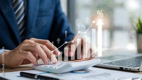 Close up of businessman in blue suit working on calculator with financial growth chart and interest rate increase