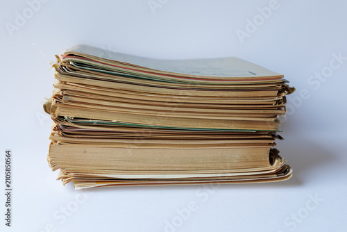 Photos Stack of aged magazines and books with yellowed pages, damaged edges and worn paper covers on a light isolated background