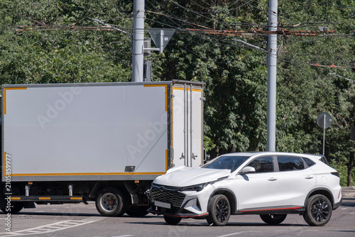 Photo of a road accident involving a white SUV and a delivery truck on a city street. Front vehicle damage, auto insurance, road safety and urban traffic concept.