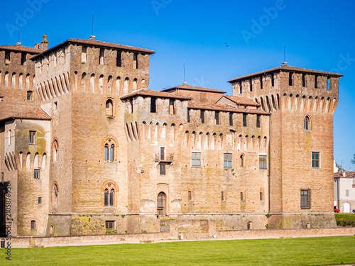 Castel San Giorgio presenting ancient medieval architecture with weathered brick walls, multiple towers, and historic details, standing on a clear day against a blue sky in Mantova, Italy
