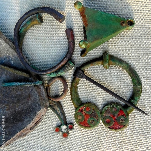 Fotografie Macro of Kiev culture bronze jewelry, ancient archaeological fibula with red enamel and bracelets close up