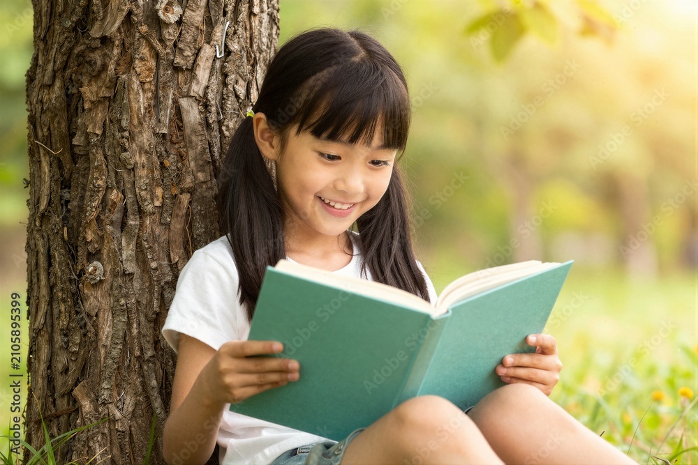 Fototapeta premium Young girl reading book while sitting under tree outdoors