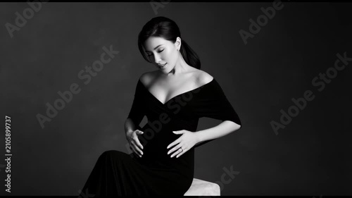 Pregnant woman sitting on a stool in a dark room during a photo session holding her belly