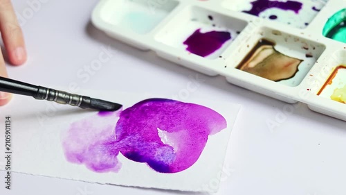 Artist painting with watercolor on paper using water to create soft texture and color effects. Close up of paintbrush blending wet paint in home studio during creative painting process