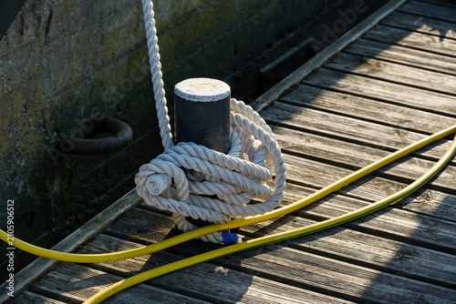 Canvastavla Thick mooring rope tied around a black metal bollard on a wooden pier