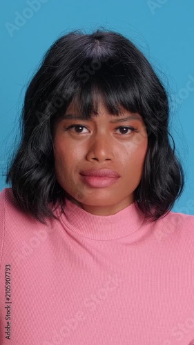 Upset Southeast Asian woman with short hair shows disappointment and sadness while sighing on a blue background. Ideal for mental health, stress, or bad news concepts in modern advertising.