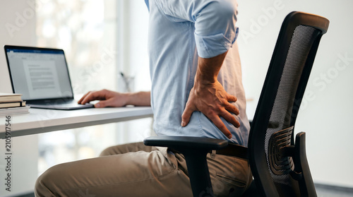 Man sitting at desk in office holding his lower back due to pain