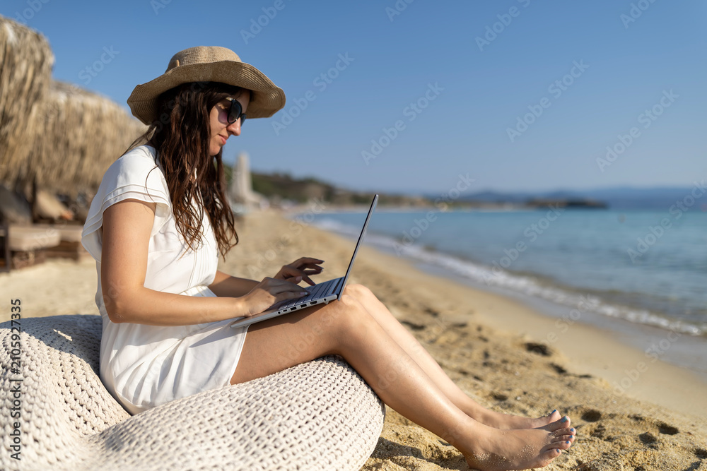 Fototapeta premium Woman working remotely on laptop by beach