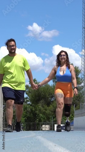 Couple holding hands while walking on an athletic track. The woman is an amputee with a prosthetic leg, demonstrating resilience and strength