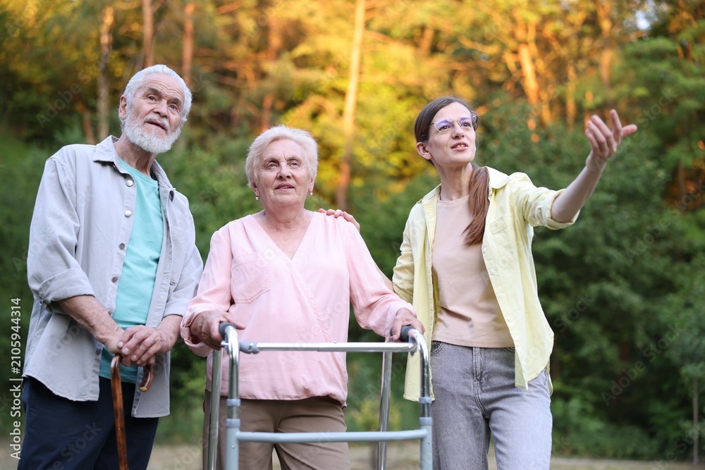 Naklejka premium Caregiver supporting elderly woman with walking frame and senior man outdoors