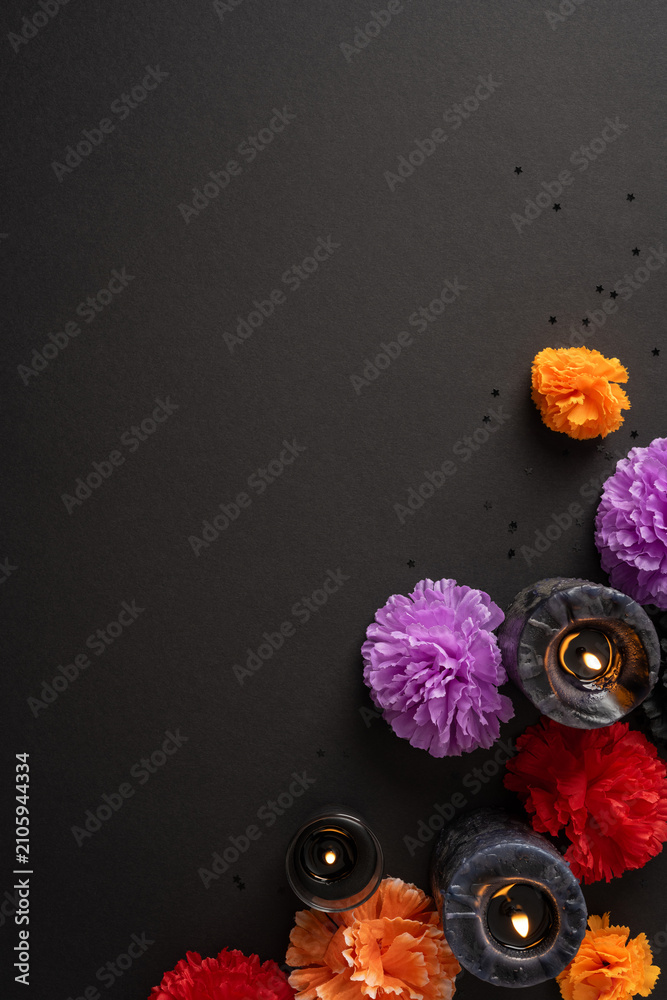 Fototapeta premium Decorative marigolds and candles for Dia de los Muertos altar on black vertical background