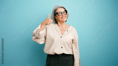 Foto Happy senior woman with gray hair and glasses smiling and showing thumbs up gest