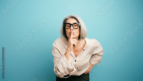 Foto Mature woman wearing glasses shushing, making a quiet gesture, symbolizing secre