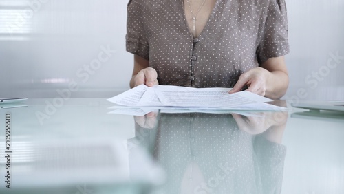 Foto Businesswoman or accountant in brawn dotted blouse is going through paperwork while holding documents at a glass desk in a well lit, contemporary office setting