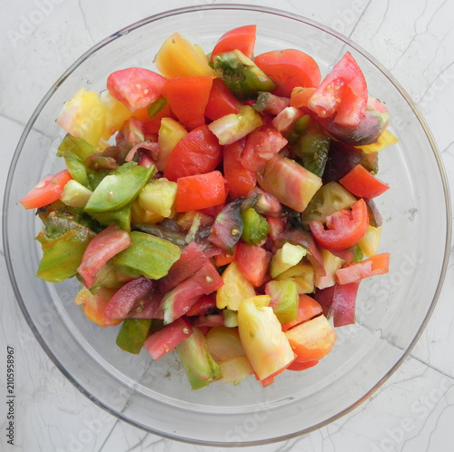 A fresh and colorful heirloom tomato salad served in a clear glass bowl. The salad consists of tomatoes of various colors including red yellow green and purple, highlighting healthy organic eating.