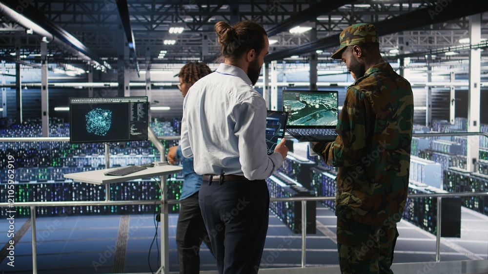 Obraz premium Military experts review a drone surveillance feed on a laptop in a data center; army units use the advanced server room for battlefield reconnaissance, intelligence software and mission operations.
