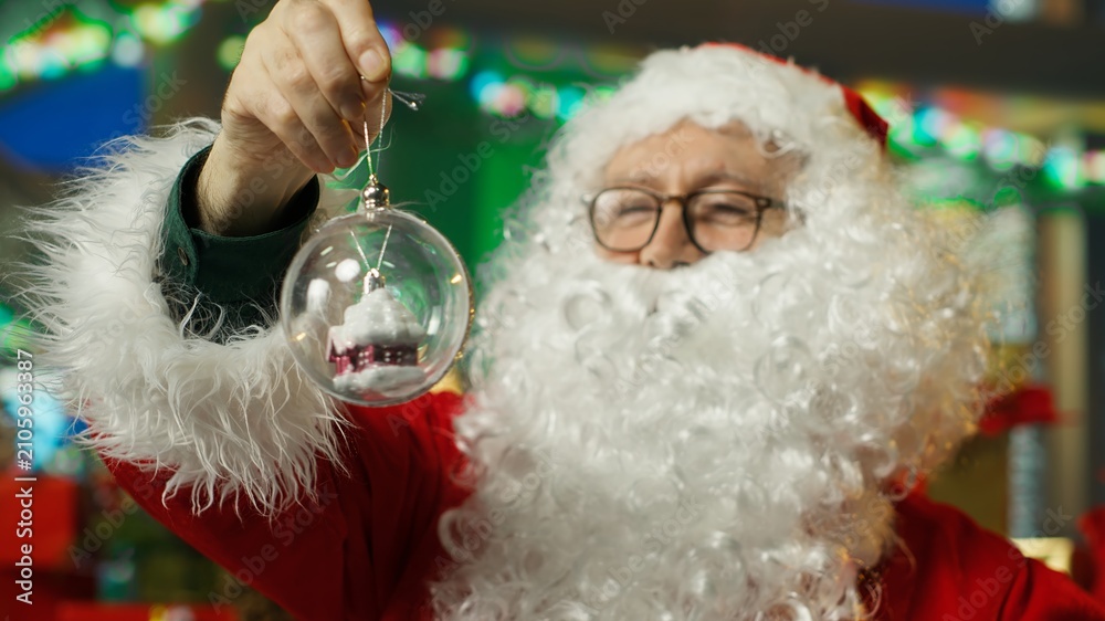 Fototapeta premium Santa Claus decorates his workshop with Christmas globes and fairytale ornaments, preparing the festive room and holiday atmosphere for visiting families during the seasonal celebration.