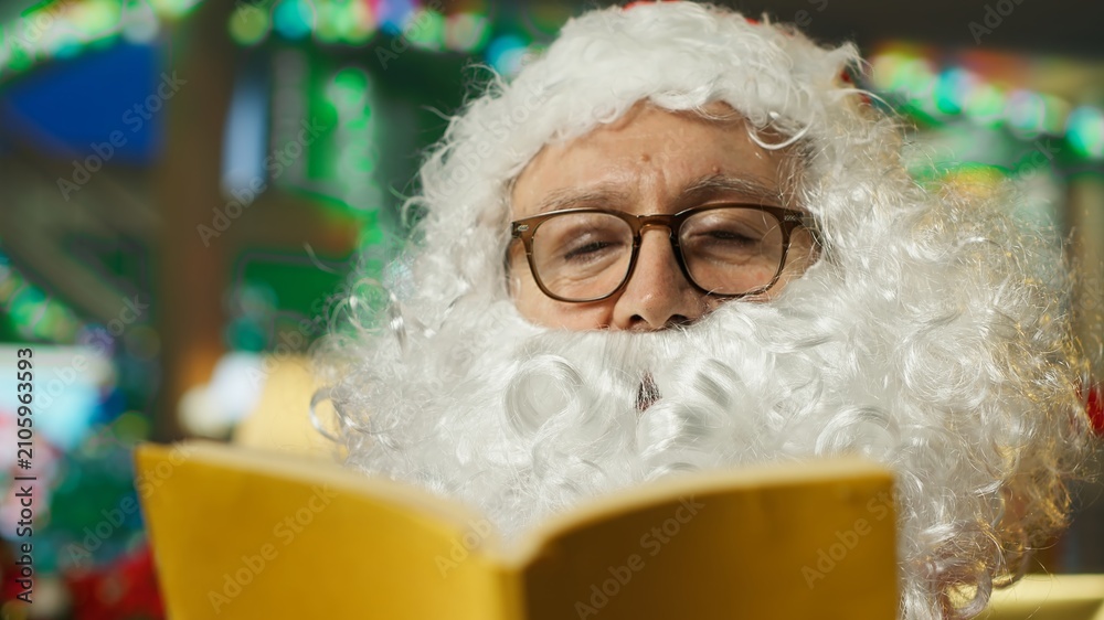Fototapeta premium A man dressed as Santa Claus reads a book to children at a charity event, narrating a holiday story that creates a sense of magic and wonder for the young audience during Christmas.